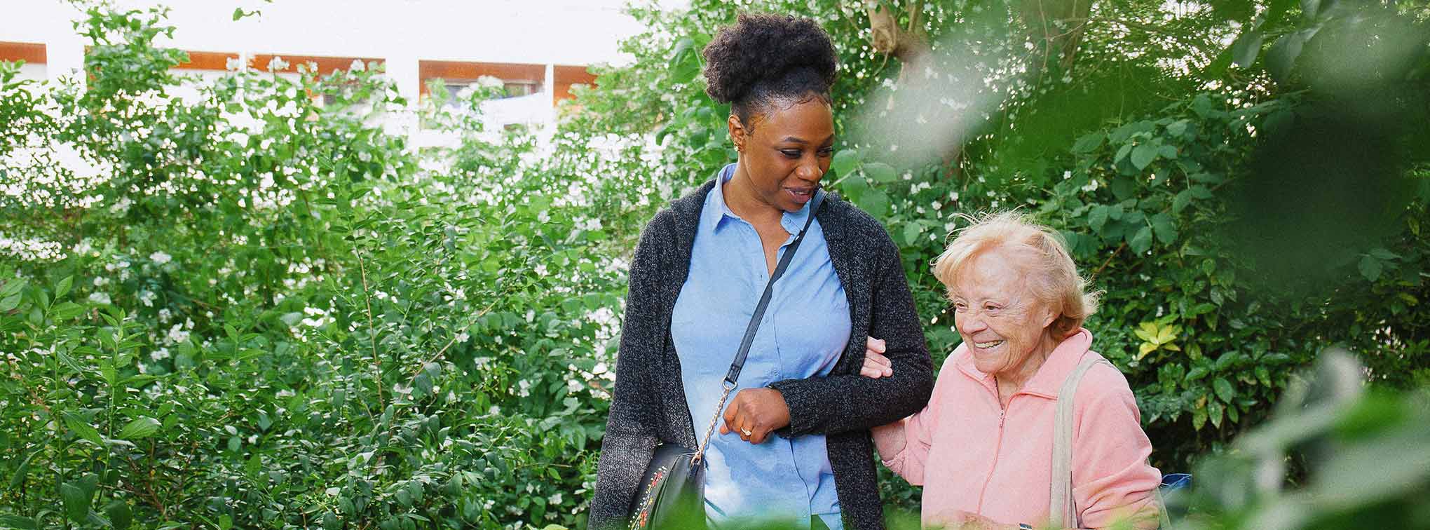 Une aide a domicile qui se promène avec une dame agée au parc