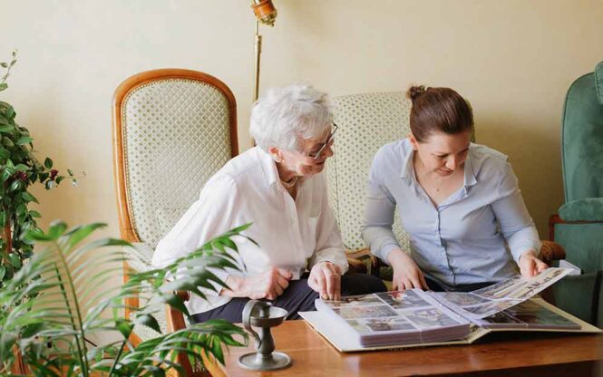 une aide a domicile regarde un album photo avec une femme agée