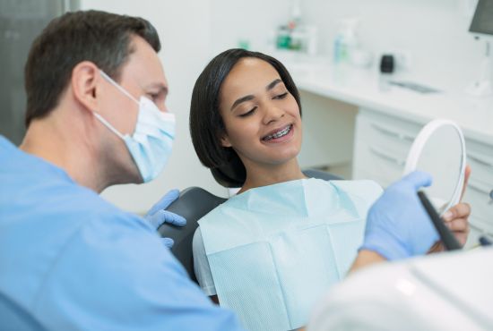 Un orthodontiste qui pose l'appareil dentaire d'une jeune patiente