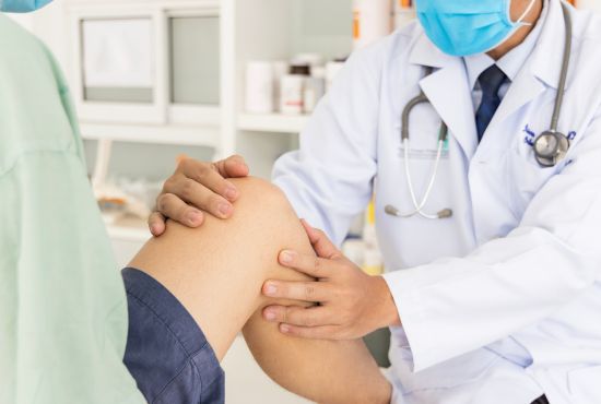 Un médecin examine le genou d’un patient lors d’une consultation médicale, illustrant un diagnostic orthopédique ou une évaluation de douleur articulaire.