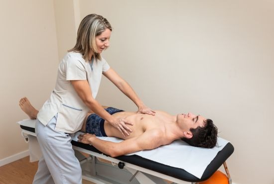 Une kinésithérapeute effectue une séance de kinésithérapie respiratoire sur un patient allongé sur une table de traitement, en utilisant des techniques manuelles pour libérer les voies respiratoires et améliorer la ventilation pulmonaire.