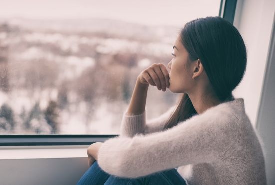 une femme regardant sa fenêtre en pleine dépression hivernale
