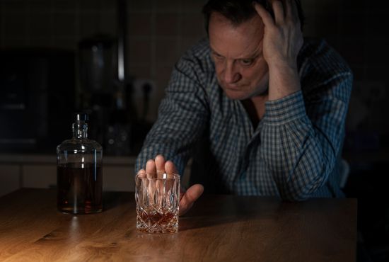 Un homme assis à une table, regardant un verre d'alcool avec une bouteille à côté, illustrant la difficulté de réduire sa consommation d'alcool et l'importance de trouver des stratégies pour y parvenir progressivement.