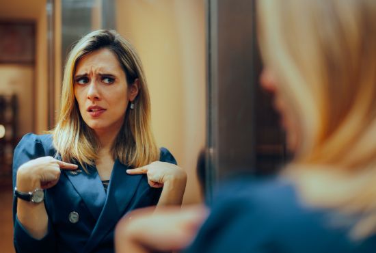 Femme se regardant dans un miroir avec doute, illustrant le syndrome de l’imposteur et le manque de confiance en soi.