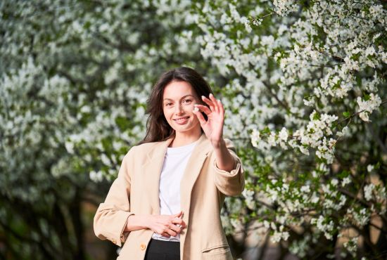 Femme tenant un comprimé antihistaminique devant des arbres en fleurs pour soulager sa rhinite allergique.