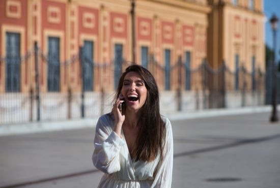 Femme souriante utilisant sa voix lors d'une conversation téléphonique en extérieur.