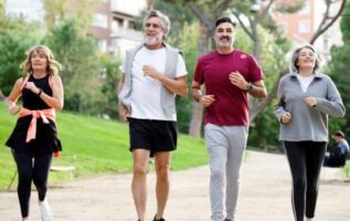 Groupe de quatre adultes pratiquant le jogging en extérieur dans un parc verdoyant.