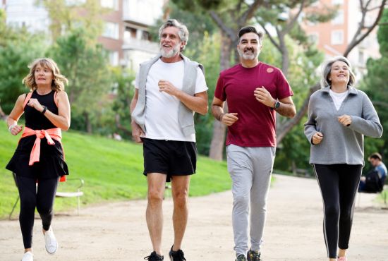 Groupe de quatre adultes pratiquant le jogging en extérieur dans un parc verdoyant.