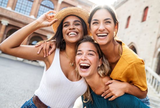 Trois jeunes femmes riant aux éclats ensemble en extérieur, illustrant les bienfaits du rire sur le lien social.