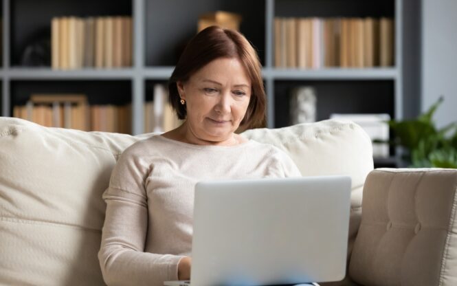 femme de 60 ans devant son ordinateur sur son canapé