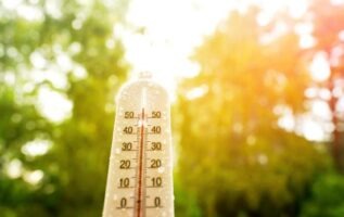 Un thermomètre extérieur couvert de gouttelettes d'eau affichant une température élevée sous un soleil de plomb et une forte luminosité.