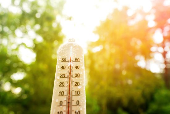 Un thermomètre extérieur couvert de gouttelettes d'eau affichant une température élevée sous un soleil de plomb et une forte luminosité.