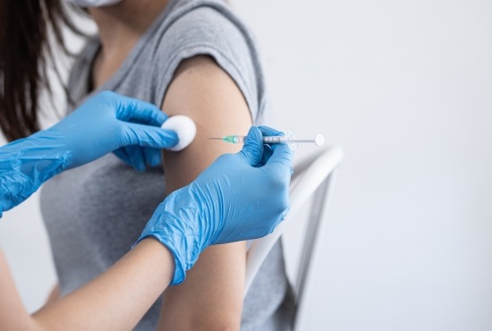 Un professionnel de santé portant des gants bleus applique un coton tout en réalisant une injection vaccinale dans le bras d'une patiente.