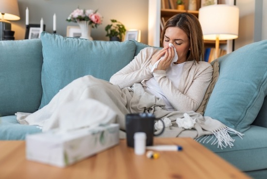 Une femme souffrant de la grippe, allongée avec un plaid et un thermomètre médical, illustrant un état grippal fébrile.