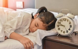 Une jeune fille dort paisiblement dans son lit à côté d'un réveil posé sur la table de chevet.
