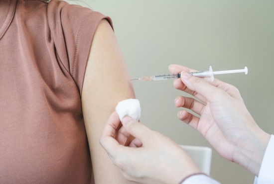 Un professionnel de santé appliquant un coton sur le bras d'une patiente tout en injectant un vaccin avec une seringue.