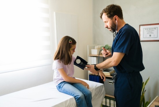 Un médecin ou pédiatre mesure la tension artérielle d'une jeune fille assise sur une table d'examen médicale avec un tensiomètre manuel.