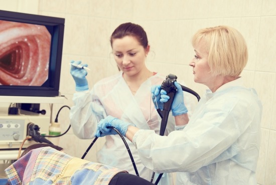 Une équipe médicale composée d'une gastro-entérologue manipulant un endoscope et d'une assistante effectuant un examen de fibroscopie digestive face à un écran de contrôle.