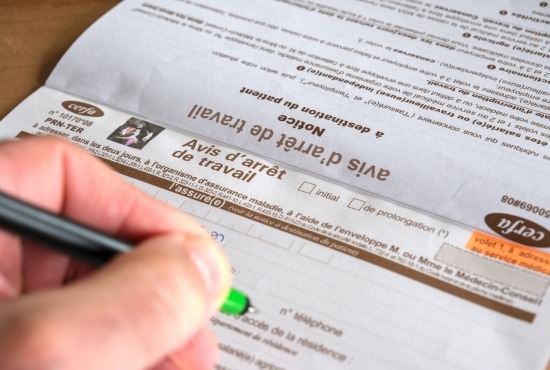 Une main tenant un stylo s'apprête à remplir un formulaire Cerfa officiel d'avis d'arrêt de travail.